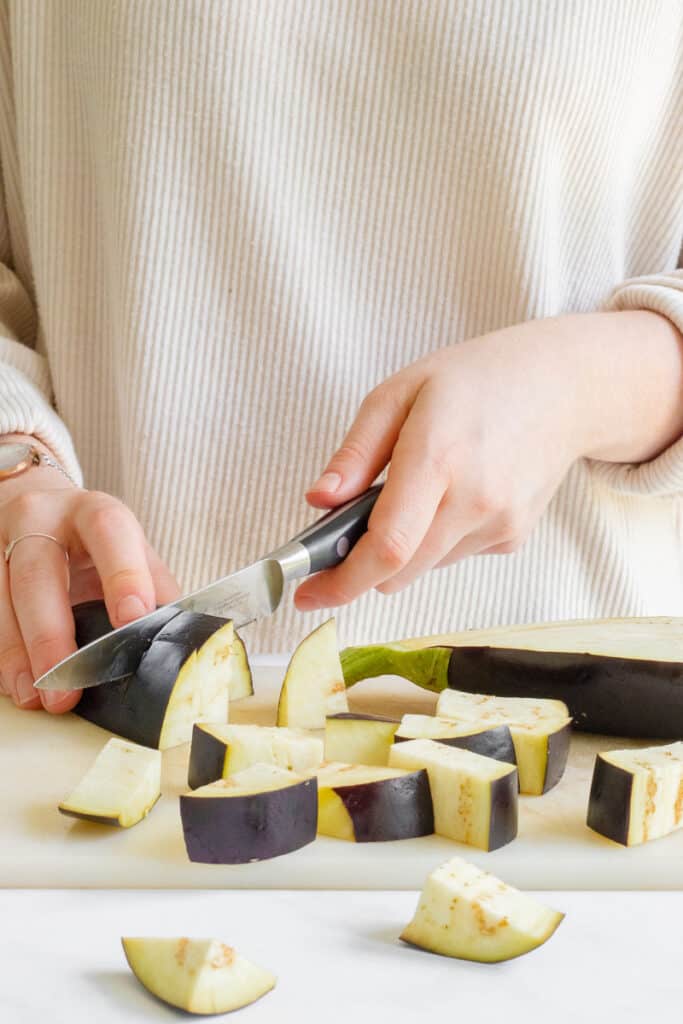 A picture of cutting up an aubergine into small chunks.