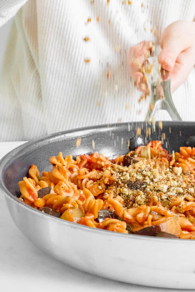 Sprinkling the almond crumb on top of the Pasta alla Norma. Vegan, GF & Healthy! Georgie Eats.