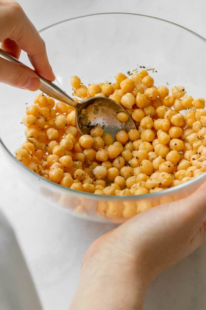 Mixing chickpeas with seasoning in a bowl.