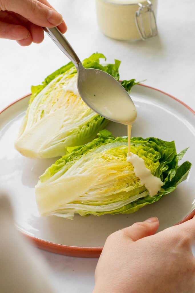 Pouring caesar dressing over little gem lettuce.
