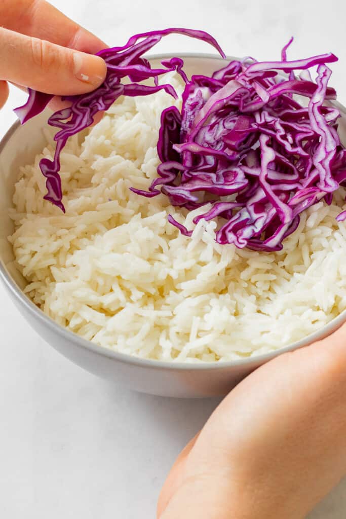 Rice being topped with red cabbage.