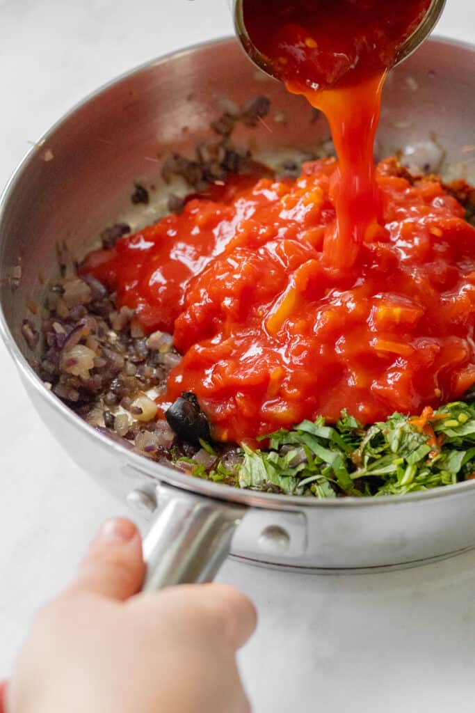 Adding the tinned tomatoes into the pan to create the pasta sauce.