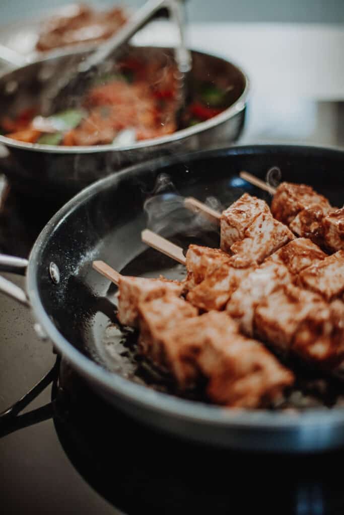 Satay tofu skewers frying in a pan.