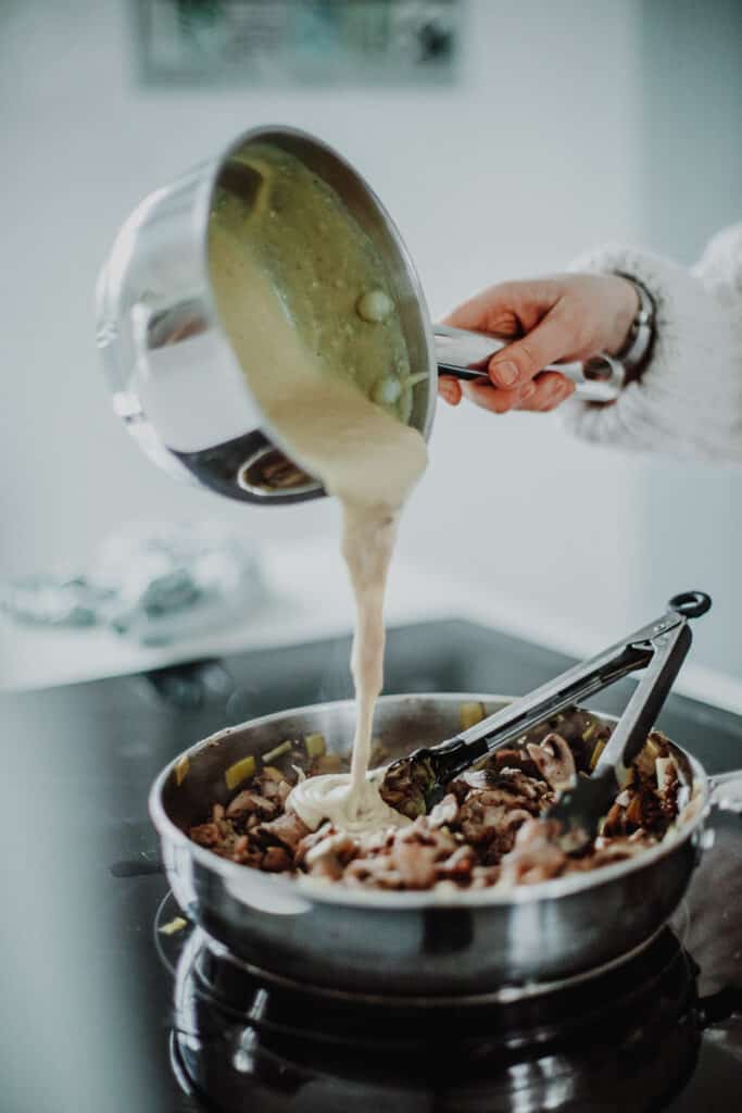 pouring the white sauce into the mushroom and leek mixture