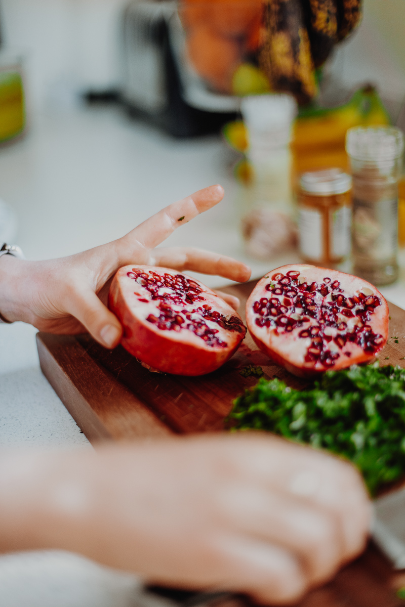 A chopping board with chopped herbs and fresh pomegranate.