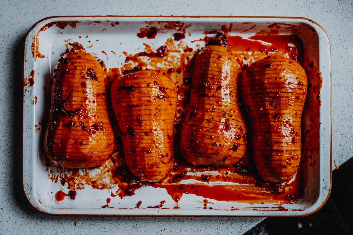 four hasslebacked squash on a baking tray