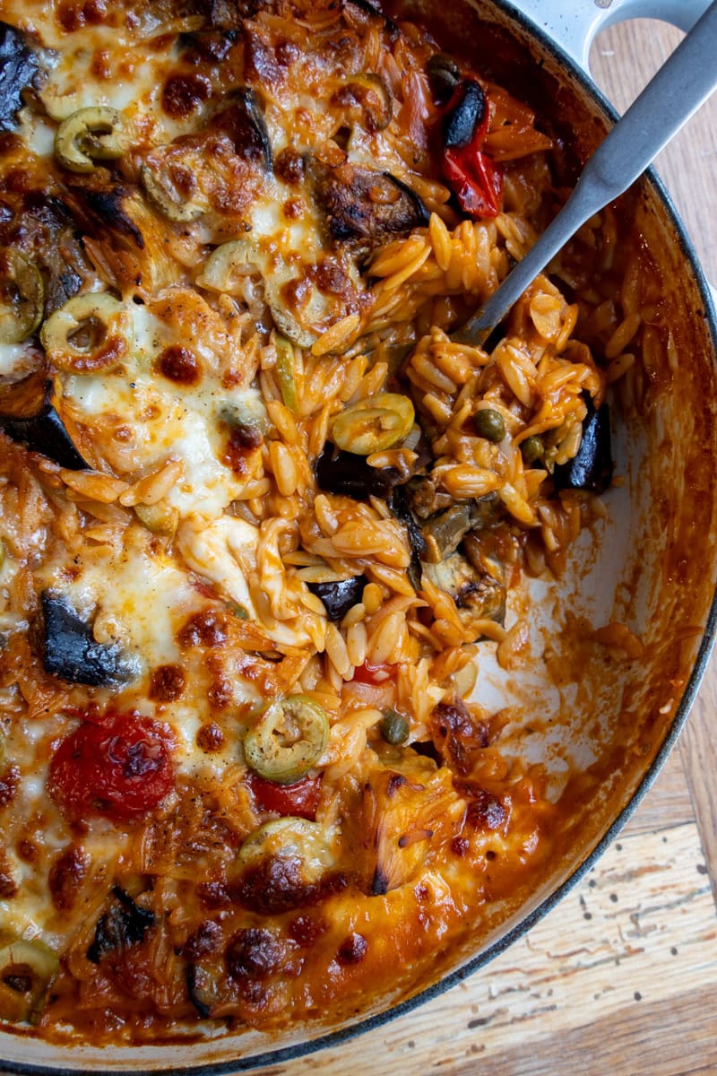 A Caponata Orzo Bake being spooned out of dish - Georgie Mullen